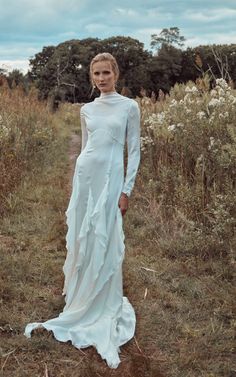 a woman in a long white dress standing in the middle of a field with tall grass