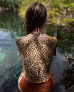 the back of a woman's body covered in tattoos sitting on top of a rock