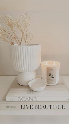 a white vase sitting on top of a stack of books next to a candle