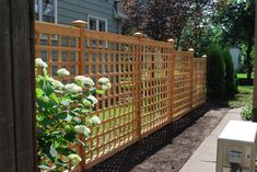 a wooden fence in front of a house with flowers growing on the top and bottom