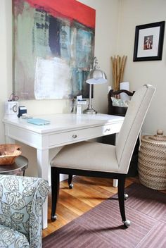 a white desk with a chair in front of it and a painting on the wall