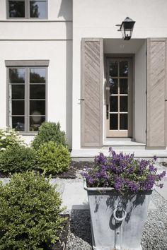 a planter filled with purple flowers sitting in front of a white building next to shrubbery