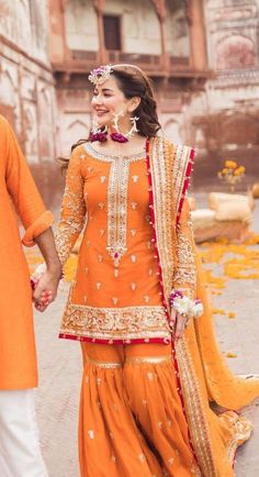 a man and woman in orange outfits holding hands while walking down the street with flowers around them