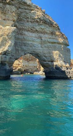 an arch in the side of a rocky cliff over water with a boat on it