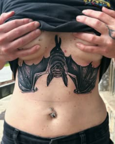 a man with a bat tattoo on his stomach holding up his shirt to the camera