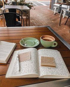 an open book sitting on top of a wooden table next to a cup of coffee