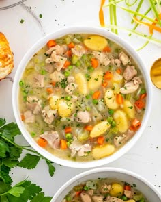 two bowls filled with chicken and dumplings next to bread on a white table top