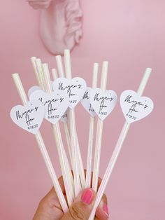 a hand holding six heart shaped straws with writing on them