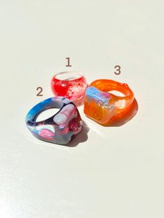 "Colorful and shiny statement rings. Each ring is one of a kind (they have different sizes). You can choose to purchase only one ring, or the three rings in the listing (Prices vary depending on the option you choose). Please select the number of the ring you want or if you would like to take all of them please click the option \"All three rings\". You will receive the exact ring/rings shown in the pictures. Ring 1 Diameter: 17 mm Ring 2 Diameter: 19 mm Ring 3 Diameter: 19 mm" Unique Clear Resin Ring, Unique Multicolor Resin Ring, Unique Clear Resin Rings, Trendy Resin Ring Jewelry, Trendy Resin Ring, Handmade Multicolor Resin Rings, Trendy Multicolor Resin Rings, Trendy Multicolor Plastic Rings, Trendy Plastic Rings As Gifts