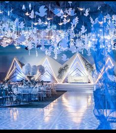 a room filled with lots of tables covered in white and blue paper cranes hanging from the ceiling