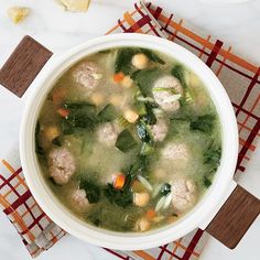 a bowl of soup with meatballs, spinach and carrots on a table