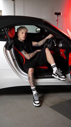 a man sitting in the driver's seat of a sports car with tattoos on his arm