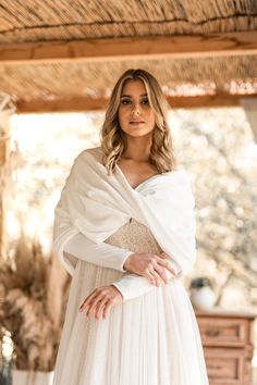 a woman wearing a white dress and shawl standing in front of a wooden structure