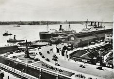 an old black and white photo of boats in the water next to a dock with cars on it