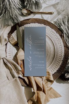 an orange menu card sitting on top of a plate next to silverware and pine branches