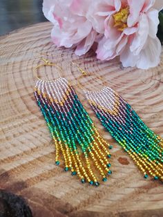 a pair of beaded earrings sitting on top of a piece of wood next to a flower