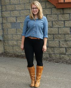 a woman standing in front of a brick wall wearing black pants and knee high boots