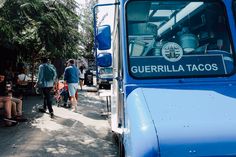 people are sitting on benches in front of a blue bus that says gurrilla tacos