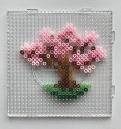 a beaded tree on a white background with pink flowers and green leaves in the center