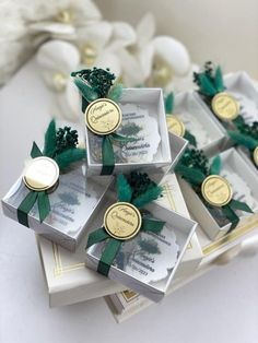 four small boxes with green ribbons on top of each box and some white flowers in the background