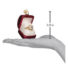 a hand holding an ornament with a ring in it's gift box