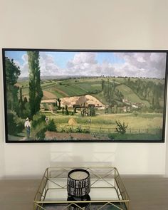 a painting hanging on the wall above a glass table with a vase in front of it