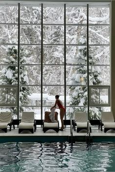 a man sitting on top of a chair next to a swimming pool in front of a large window