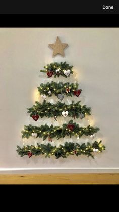 a small christmas tree with lights and ornaments on it's sides in front of a white wall