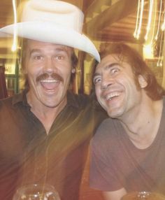 two men sitting next to each other at a table with drinks in front of them