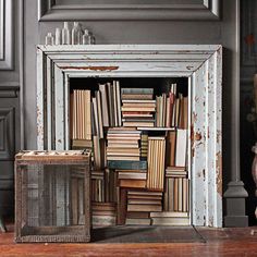 a pile of books sitting on top of a wooden floor next to a white fireplace