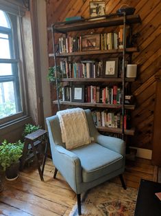 a blue chair sitting in front of a book shelf filled with books next to a window