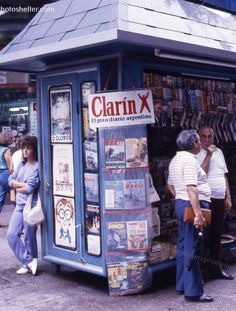 an old photo of people standing in front of a book stand that has many books on it