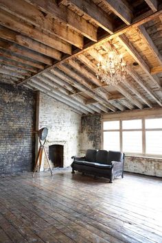 an empty living room with wood floors and exposed beams on the ceiling is lit by a chandelier