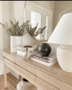 a table topped with books and a vase filled with plants next to a lamp on top of a wooden table