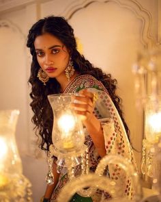 a woman is holding a glass vase with candles in it and looking at the camera