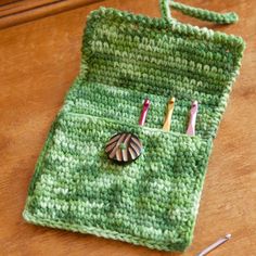 a green crochet bag with pins and needles in it on a wooden table