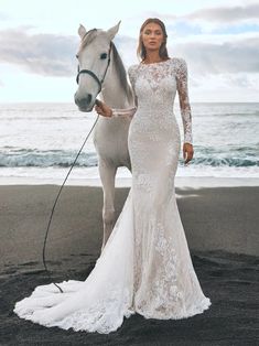 a woman standing next to a white horse on the beach with waves in the background