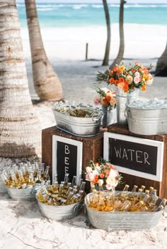 there are many bottles and buckets on the beach with flowers in them, along with wine glasses