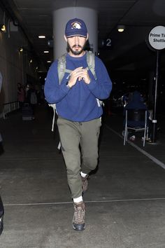 a man walking through an airport with his backpack over his shoulder and wearing a hat