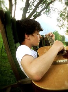 a young man sitting in a chair playing an acoustic guitar