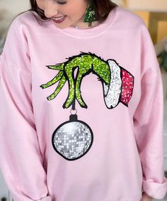 Get ready to make a bold and festive statement with our "Faux Sequin Grinch Hand Sweatshirt." This eye-catching sweatshirt features a playful graphic of the Grinch's hand dangling a disco ball, with faux sequins providing a dazzling and fun touch. Please note that the sequins are a graphic representation and are not real, ensuring comfort and ease of wear. Grinch Hand, Grinch Shirt, Grinch Hands, Sequin Design, Disco Ball, Holiday Gathering, Grinch, Festival Season, Graphic Tee