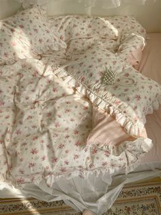 an unmade bed with pink and white flowers on it, in a bedroom setting