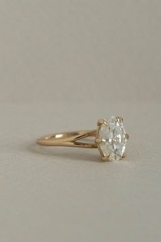 a yellow gold engagement ring with a single diamond in the center, sitting on a plain surface