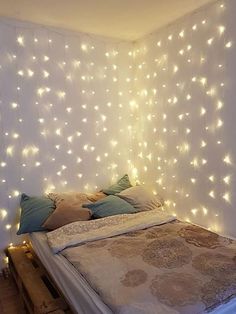 a bed that has some lights on the headboard and pillows in front of it