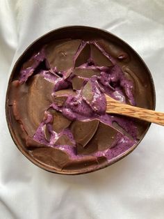 a wooden spoon in a bowl filled with chocolate and purple toppings on a white cloth