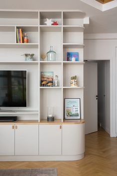 a living room with white shelving and wood flooring on the walls, along with a flat screen tv