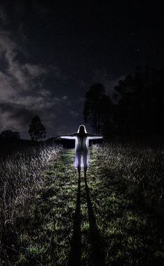 a woman standing in the middle of a field at night with her arms spread out