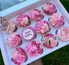 a box filled with pink cupcakes on top of a grass covered field next to a window