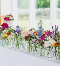 a row of vases filled with colorful flowers on top of a long white table