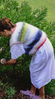 a woman picking flowers from a bush in the grass with her hand on top of it